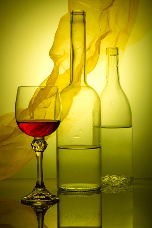Free Styled glass of red wine with empty bottles on colorful backdrop. Stock Photo