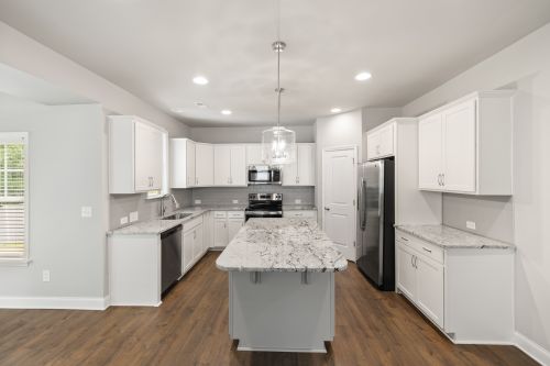 Free A spacious modern kitchen featuring white cabinets and a large granite island. Stock Photo