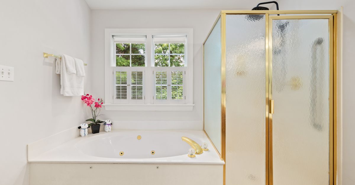 Bright bathroom featuring a luxurious bathtub and glass shower with gold accents.