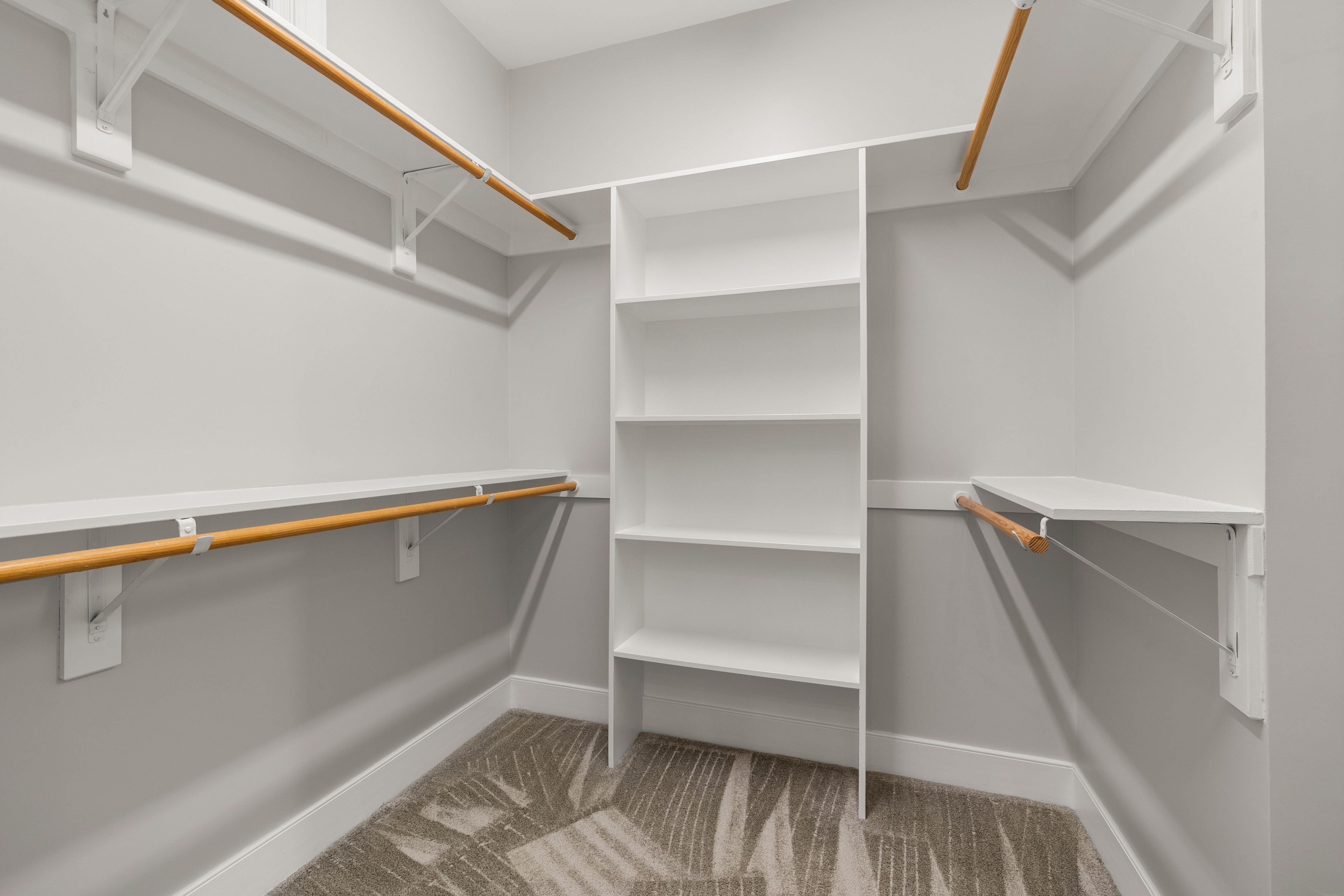 Empty modern walk-in closet with white shelves and wooden rods, ideal for organization.