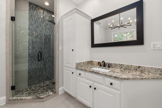 Spacious modern bathroom featuring a granite countertop vanity and elegant glass shower.