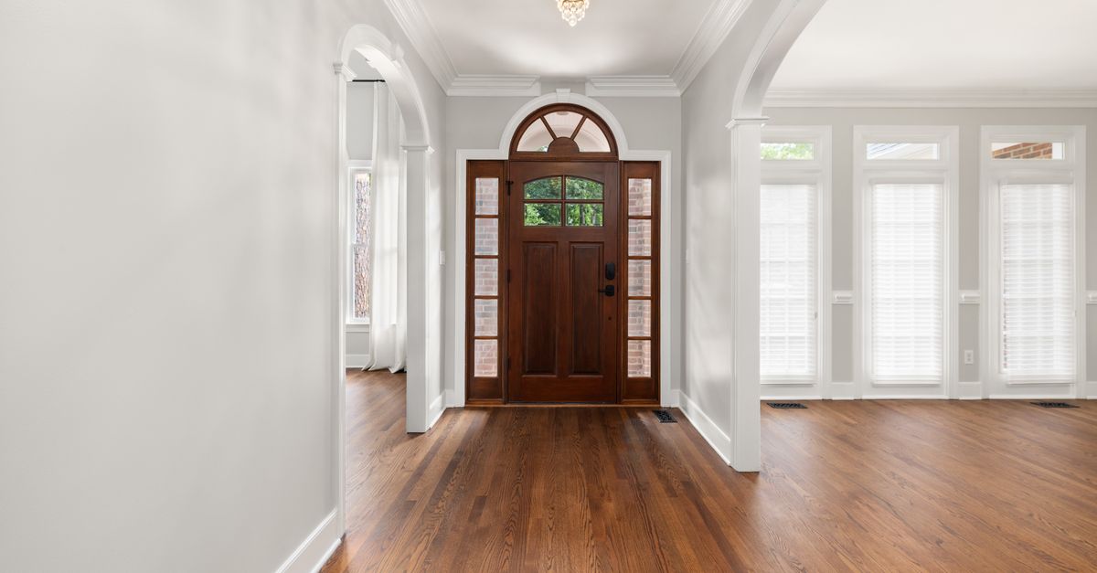 Spacious entrance hall with a wooden front door, hardwood floors, and large windows.