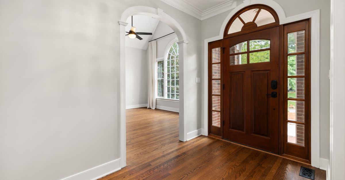 Bright and elegant foyer featuring a large arched wooden door with sidelights and a view into a living area.