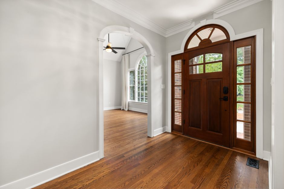Bright and elegant foyer featuring a large arched wooden door with sidelights and a view into a living area.