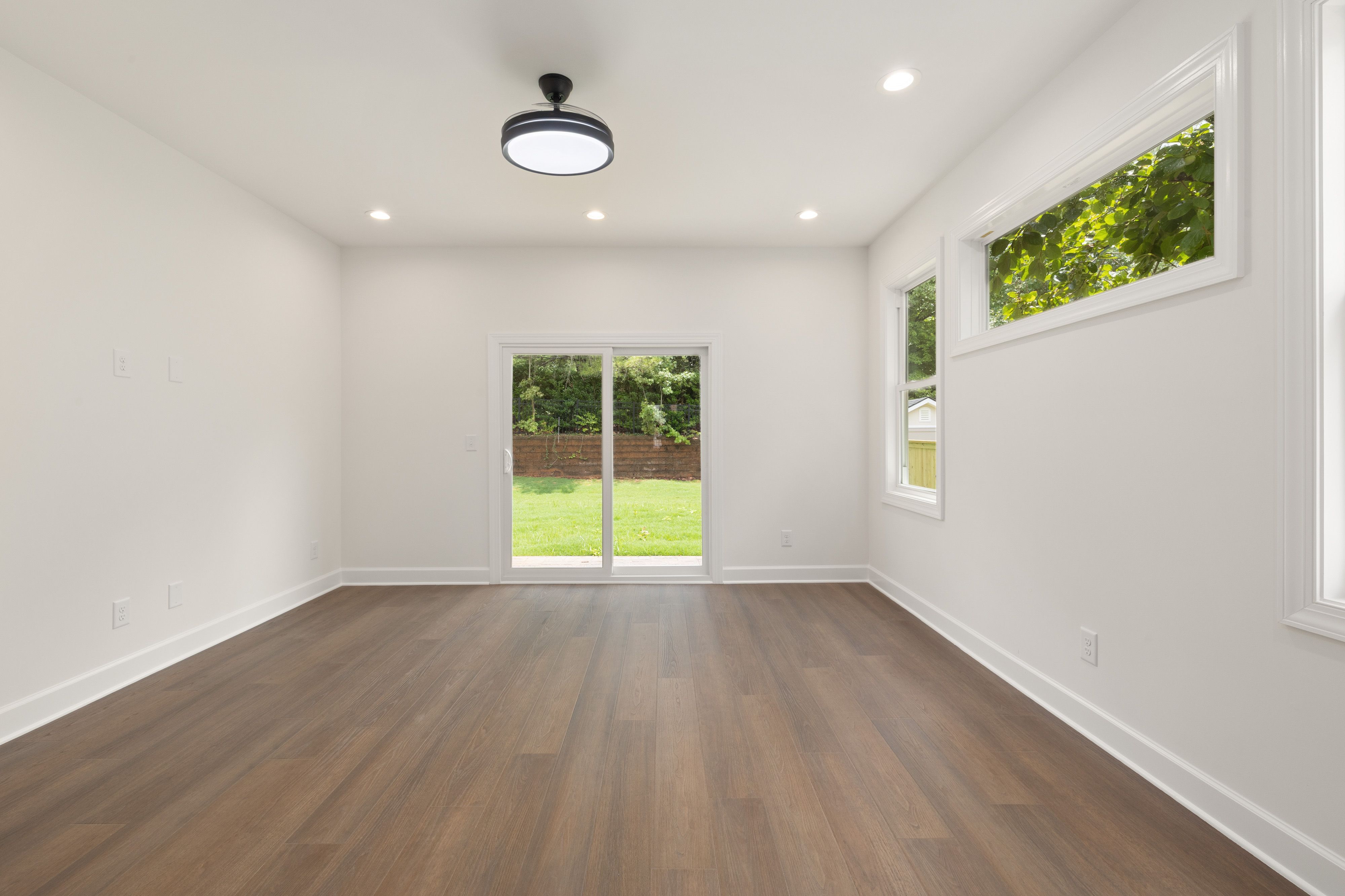 Bright empty room with wooden flooring and sliding glass doors leading to a garden.