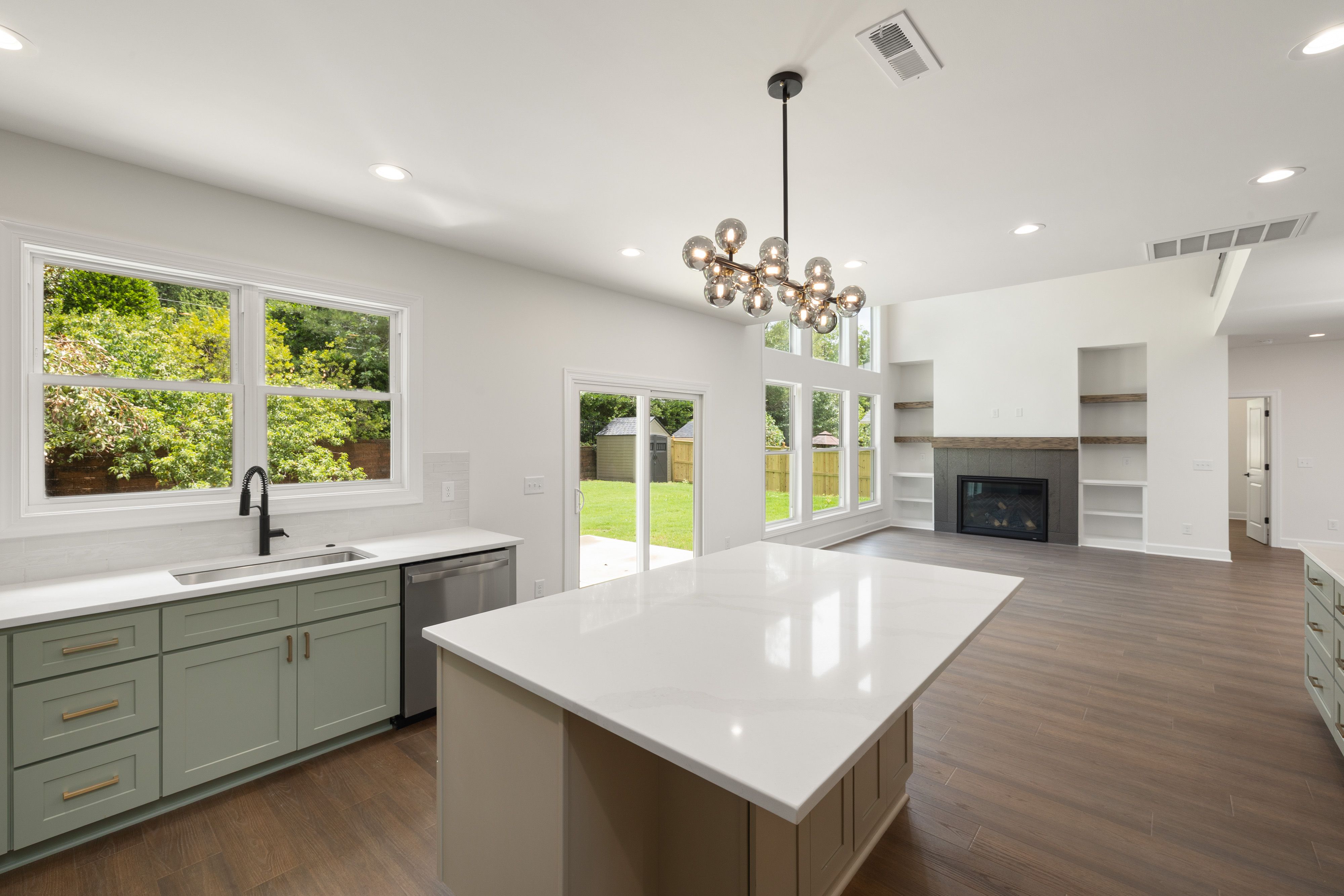 Bright modern kitchen with island, white cabinets, large windows, and open view to living room and backyard