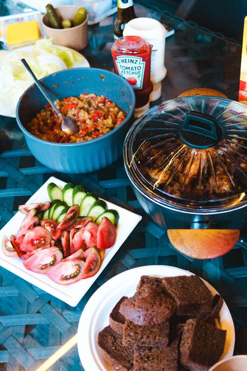 Free Colorful summer picnic setup with fresh vegetables, sauces, and brown bread on a glass table. Stock Photo