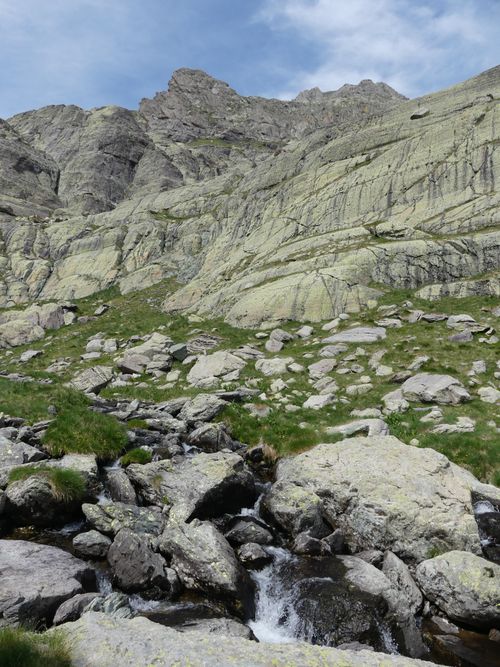 Free A serene rocky mountain landscape featuring a small stream flowing amidst lush greenery and rugged cliffs. Stock Photo