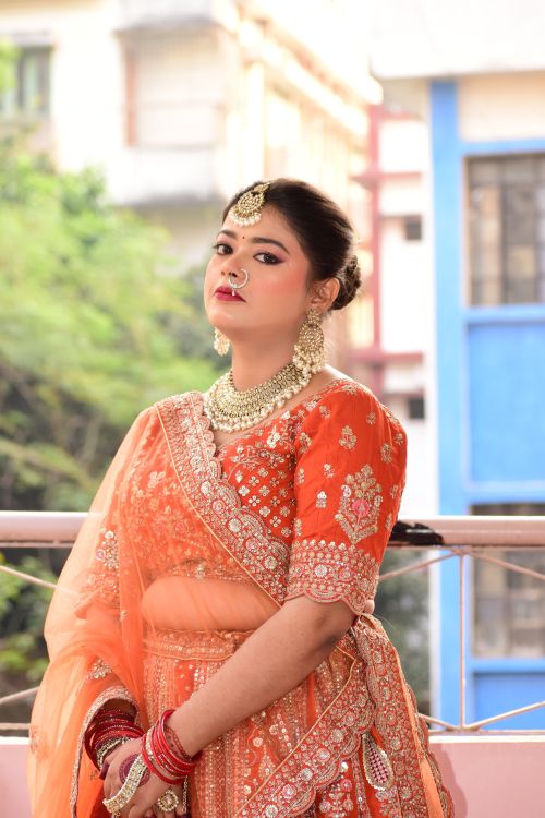 Free A South Asian woman in a vibrant orange traditional dress poses outdoors. Stock Photo