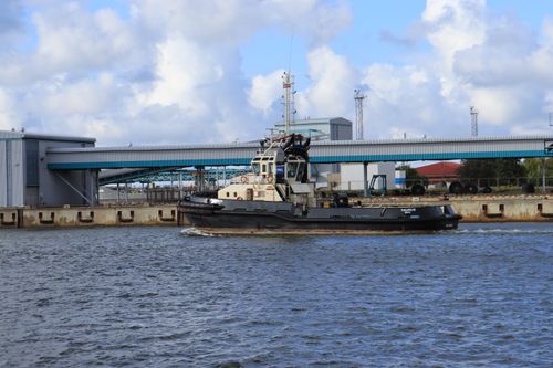 Free A tugboat sails past industrial structures on a sunny day, highlighting maritime and industrial themes. Stock Photo