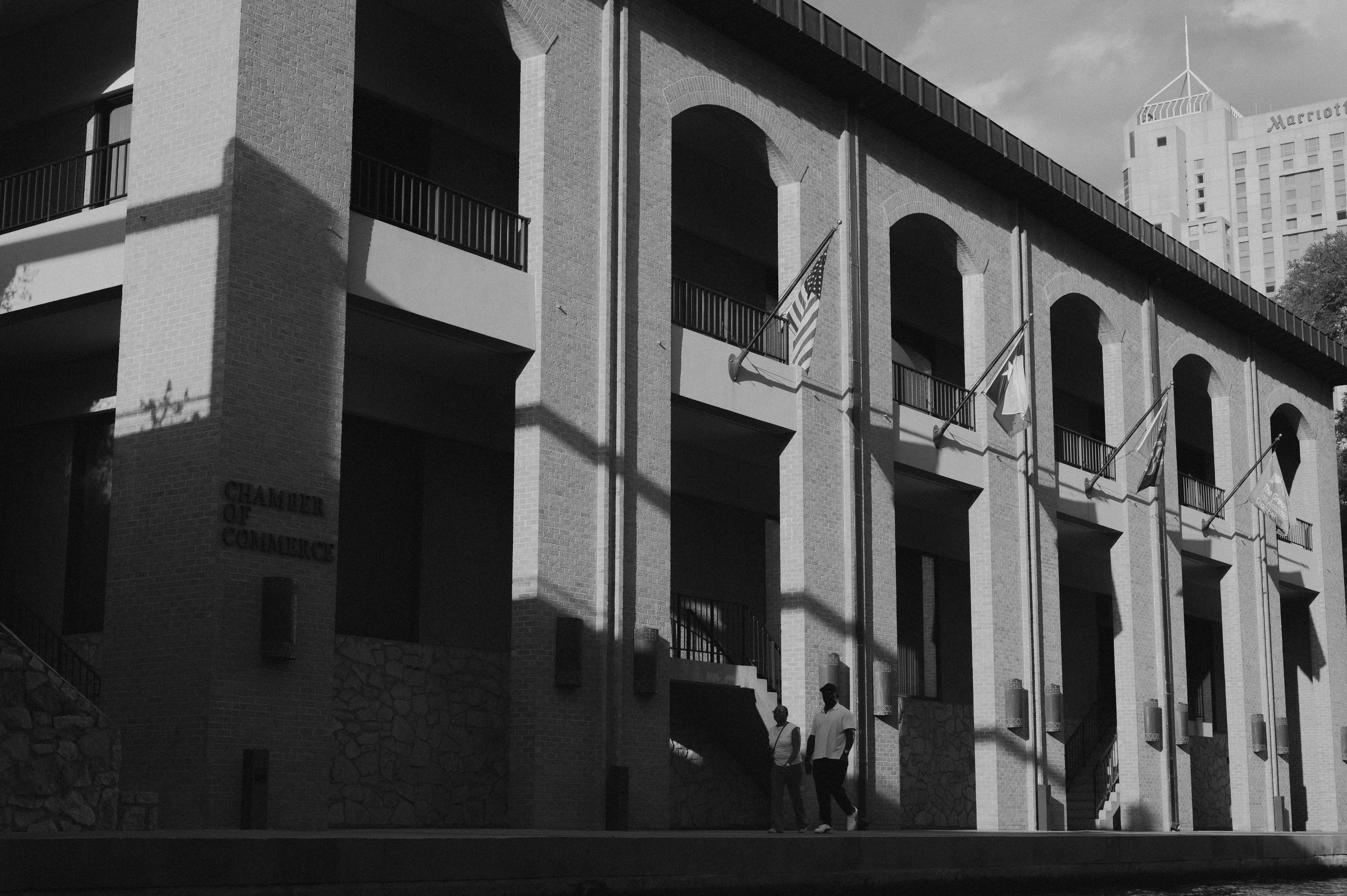 Black and white photo capturing architectural shadows on a building facade with two people walking.