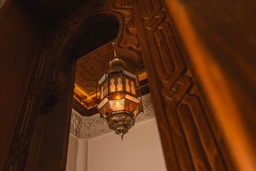 Free Beautifully crafted Moroccan lantern hanging amidst intricately carved wooden architecture, emitting a warm glow. Stock Photo