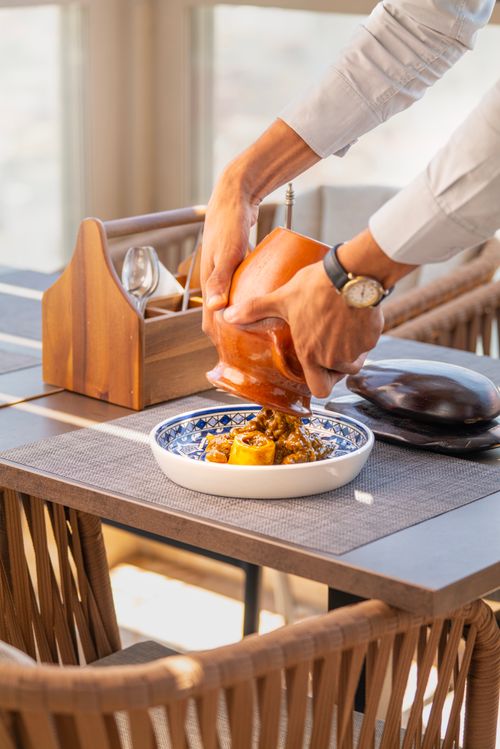 Free Close-up of person serving a homemade dish into a blue-patterned bowl on a dining table. Stock Photo