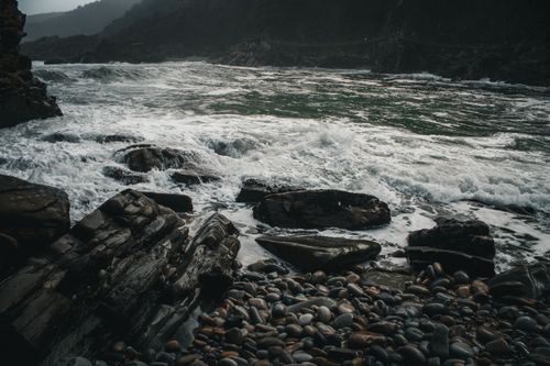 Free Moody and dramatic rocky coast with waves crashing against stones on a cloudy day. Stock Photo