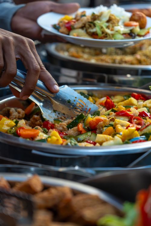 Free Hand serving colorful buffet dish with vegetables and tongs, culinary variety. Stock Photo
