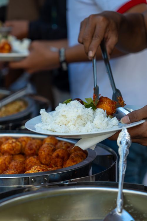Free A buffet plate with rice and meatballs being served by a person with tongs at an outdoor event. Stock Photo