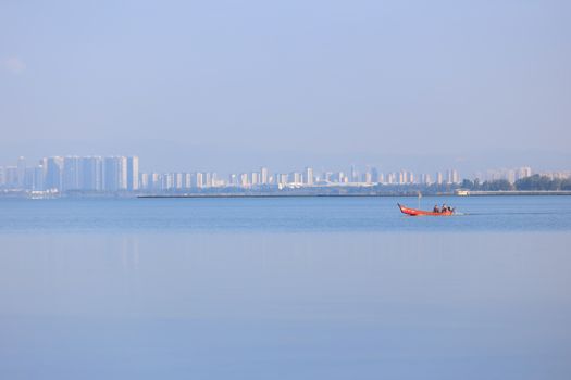 Red boat on calm lake with misty urban skyline in distance