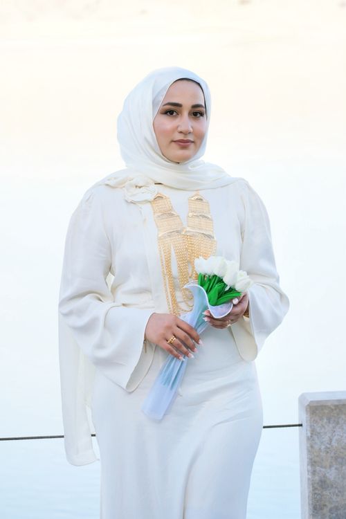 Free A woman in a white dress and hijab holding flowers, standing elegantly. Stock Photo