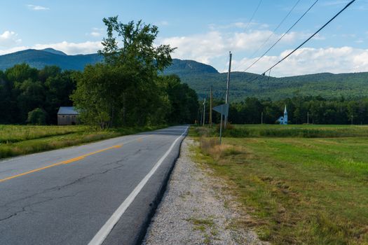 Quiet rural road with mountain view, surrounded by nature's greenery under a clear blue sky.