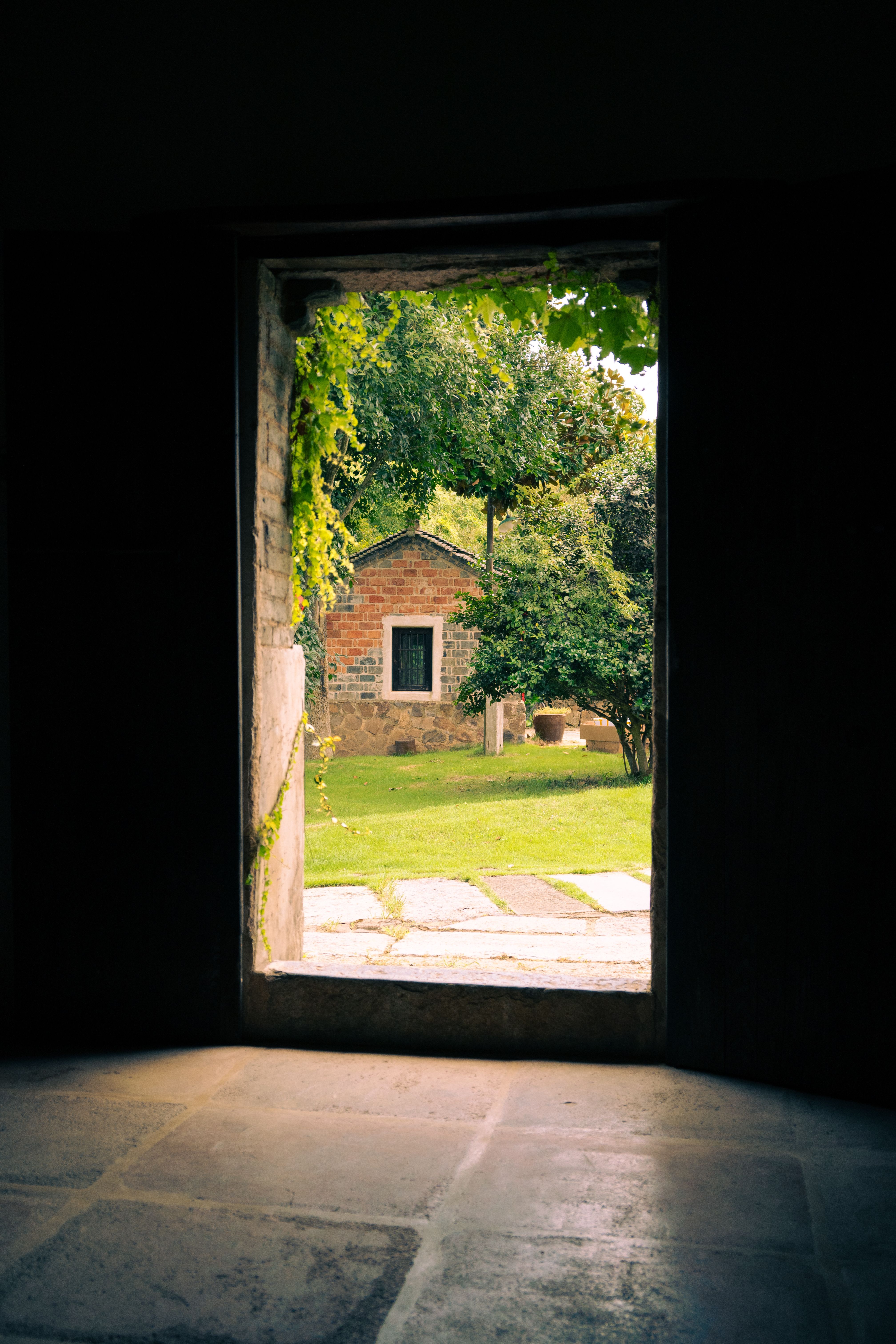 A serene view of a rustic stone house through an archway, surrounded by greenery.