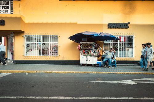 Free Street vendor sitting under umbrella in Trujillo with vibrant yellow wall. Stock Photo