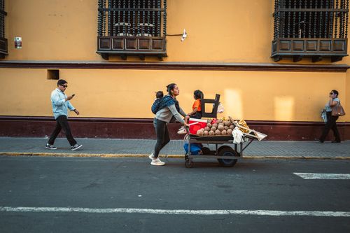 Free A woman pushes a cart with coconuts on a sunny street in Trujillo, Peru. Urban daily life scene. Stock Photo