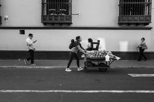 Free A street vendor pushes a cart of fruits in a historic city setting. Stock Photo