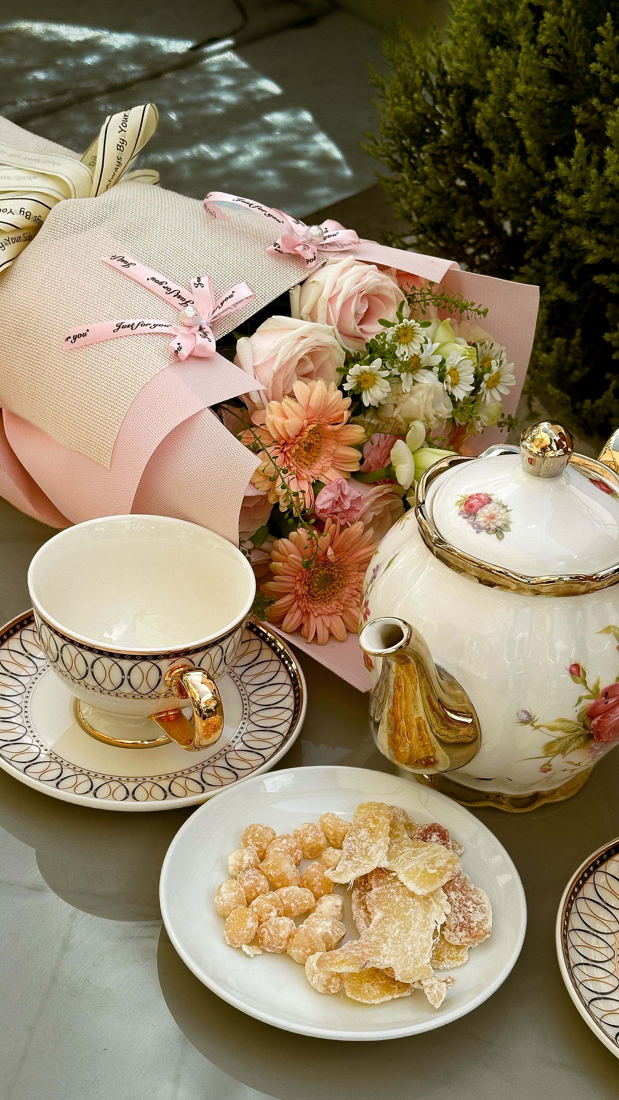 Charming tea set arrangement with flowers and sweets, perfect for an outdoor afternoon tea setting.