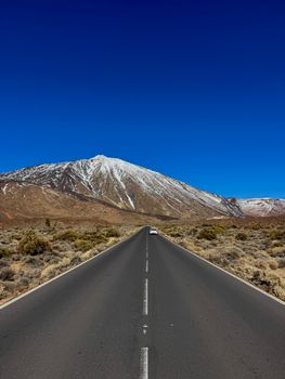 Straight road leading to snow-capped Mount Teide under a clear blue sky in Tenerife, Spain.