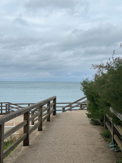 Free A peaceful boardwalk leading to the serene sea, under a cloudy sky. Stock Photo