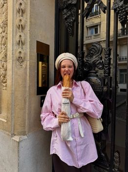 Smiling woman in a pink shirt holding a baguette in a French street setting.