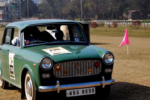 Free A classic green car participating in an outdoor rally with a pink flag on a sunny day. Stock Photo