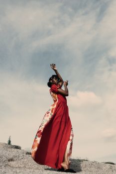 A woman in a vibrant red dress dances gracefully against a blue sky in Nigeria.