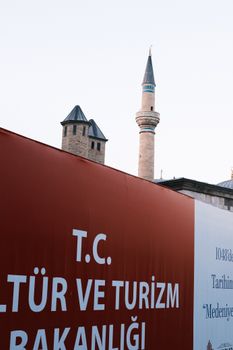 Photo of mosque minarets behind a Turkish tourism sign in an urban setting.