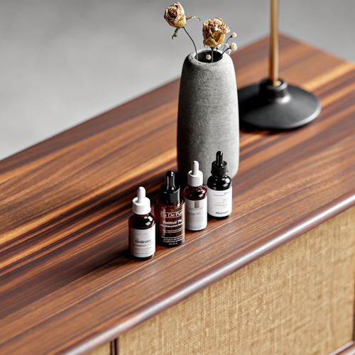 Free Modern minimalist setup showcasing skincare serum bottles on wooden furniture with natural lighting. Stock Photo
