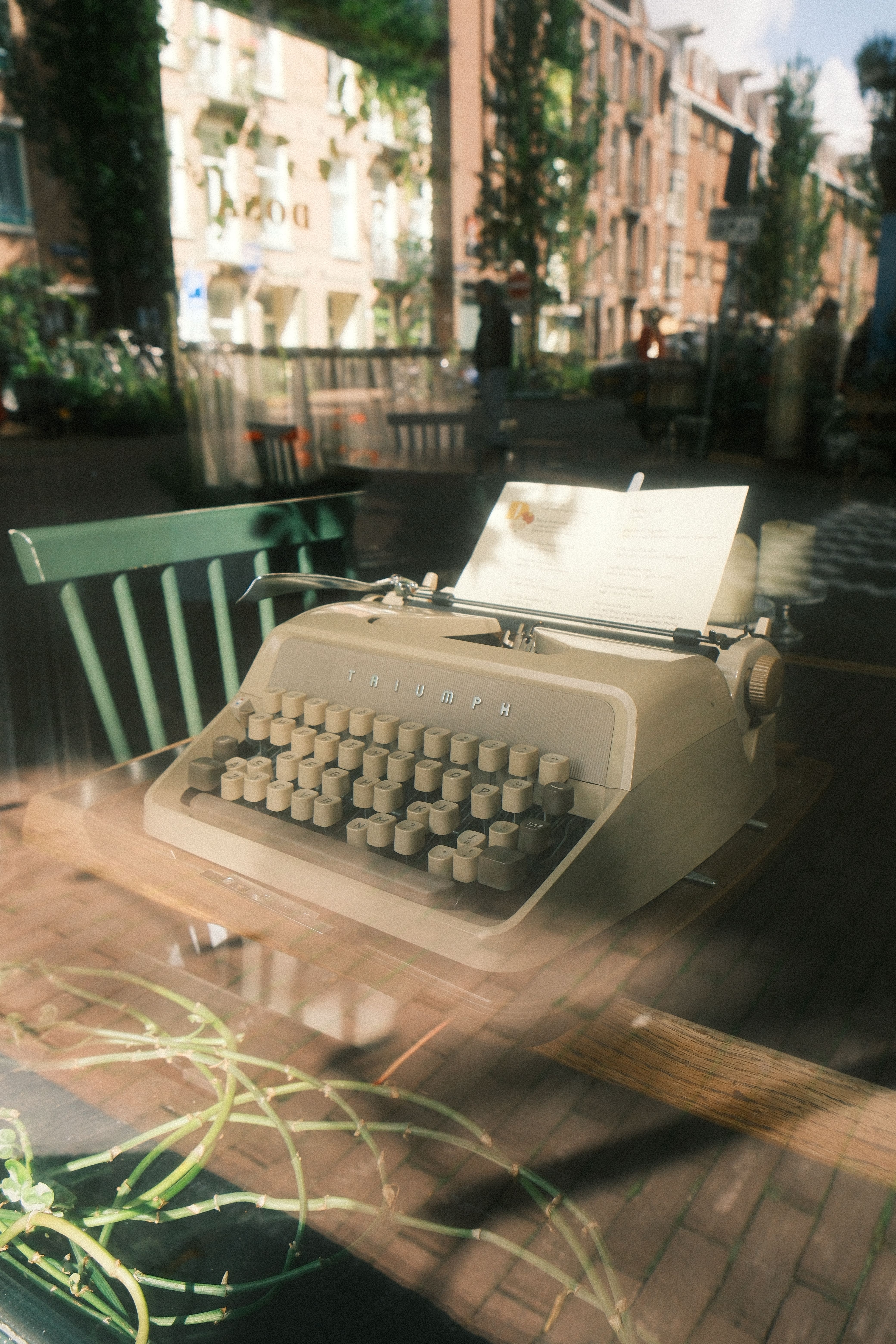 A vintage typewriter sits in an Amsterdam cafe window, reflecting charming street views.