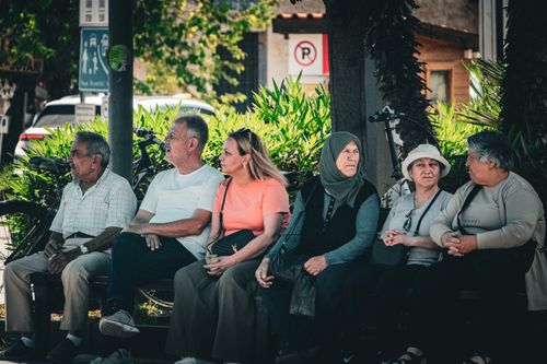 Free A diverse group of adults sitting on a bench outdoors, enjoying a sunny day and conversing. Stock Photo