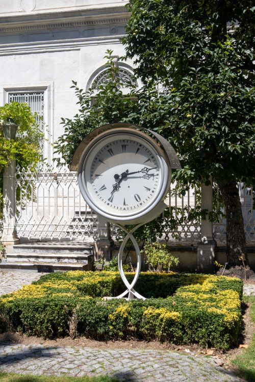Free An elegant clock stands amid lush greenery in an İstanbul garden under bright sunlight. Stock Photo