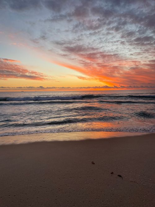 Free Captivating beach sunset with vibrant skies and tranquil waves reflecting on the water. Stock Photo