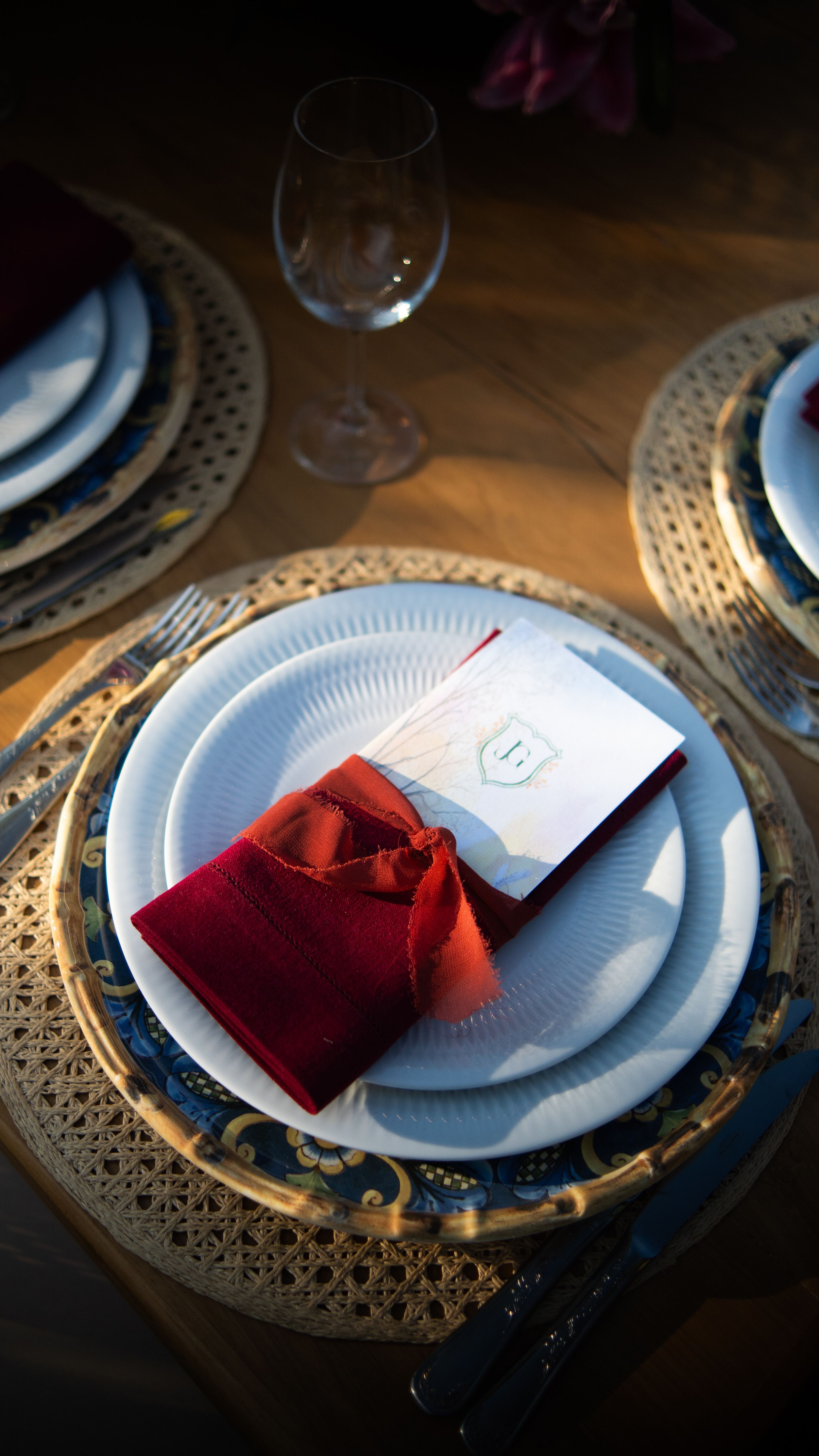 Uma mesa elegantemente posta com um prato, guardanapo vermelho, talheres e um copo sob uma luz quente.