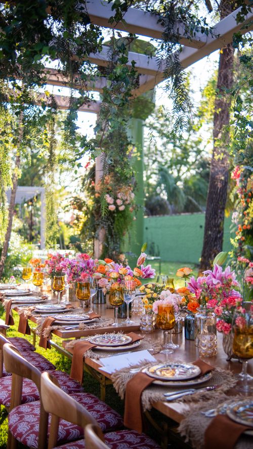 Free Long outdoor table with vibrant floral centerpieces under pergola in lush garden setting. Perfect for celebrations. Stock Photo
