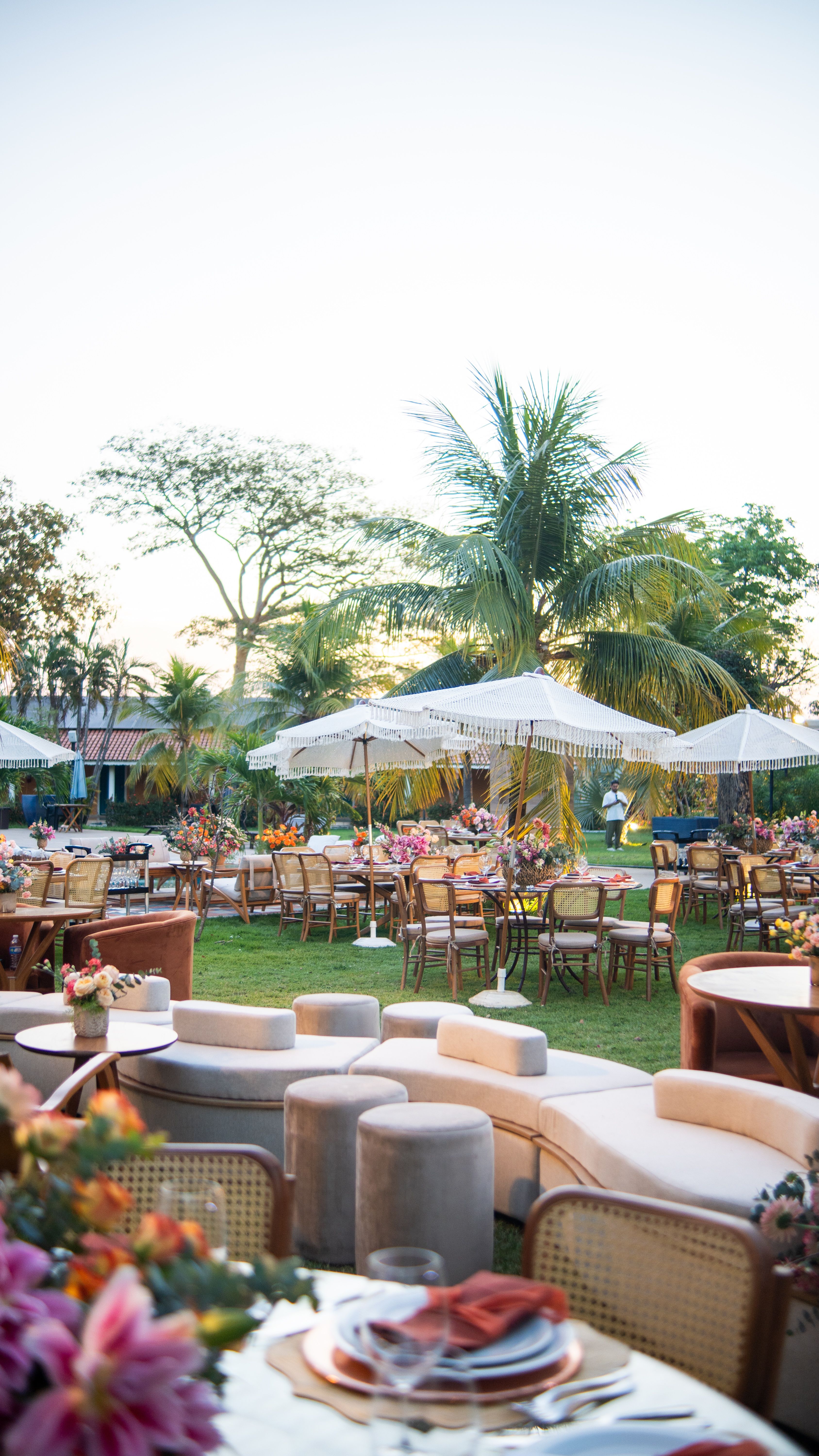Elegant outdoor tropical event with floral arrangements, parasols, and wicker furniture.