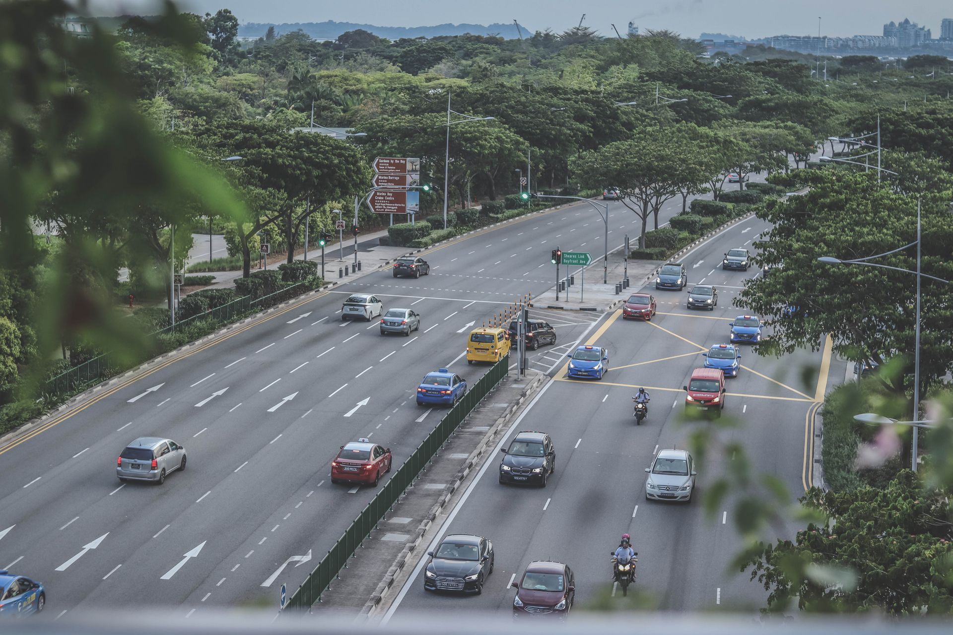 Aerial view of a busy highway with vehicles and lush greenery in an urban setting.