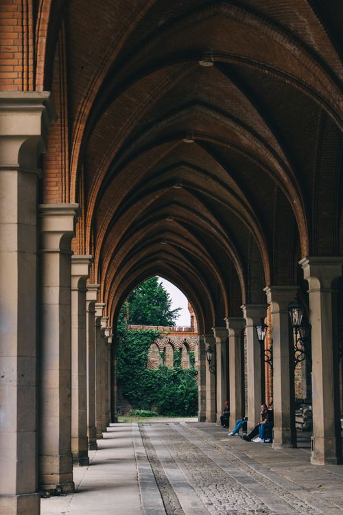 Free A serene view of a majestic brick archway with people resting on benches. Stock Photo