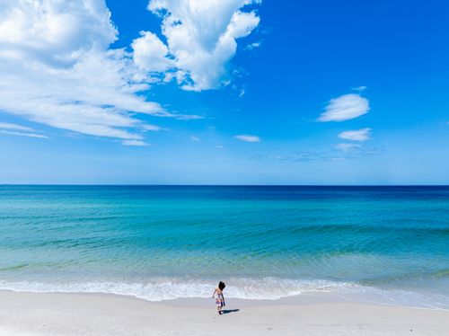 Free A child strolling on a tranquil sandy beach with clear blue skies and ocean waves. Stock Photo