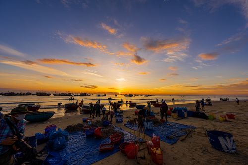 Free Fishermen at a coastal market gather their catch at sunset, vibrant sky in view. Stock Photo