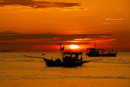 Free Fishing boats silhouette against vibrant sunset on the ocean horizon. Stock Photo