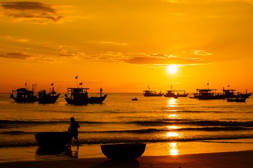 Free Serene sunset with boats silhouetted against a vivid orange sky, reflecting on peaceful waters. Stock Photo