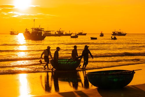 Free Silhouetted fishermen with boats at sunrise on a coastal beach. Stock Photo