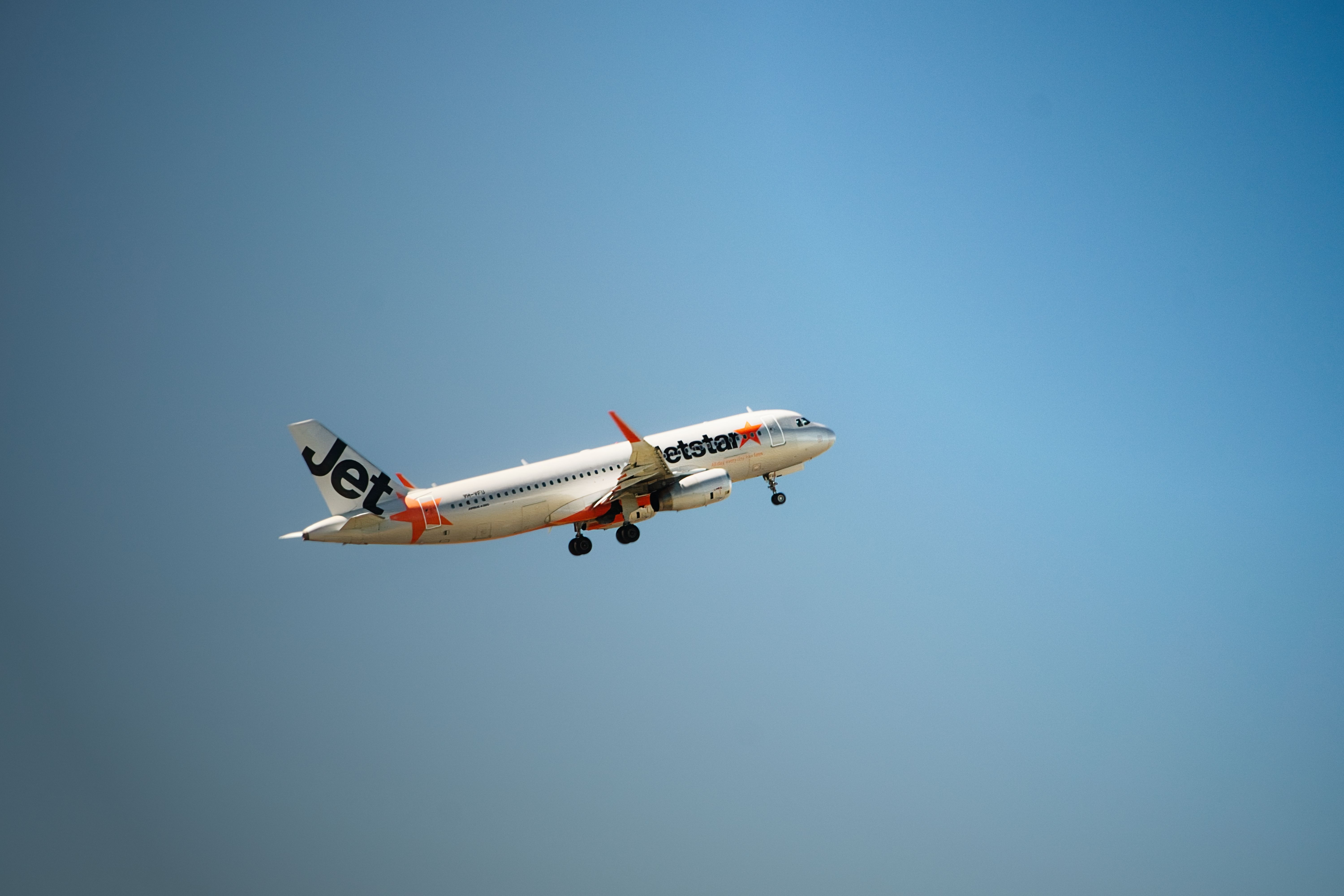 Jetstar airplane flying mid-air with clear blue sky backdrop